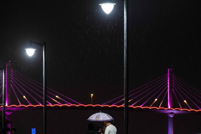 People share an umbrella on a rainy night in Basra on April 20, 2026. (Photo by HUSSEIN FALEH / AFP)