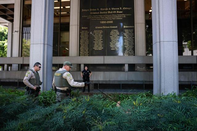 A Los Angeles sheriff and his dog search for a suspected bomb outside Los Angeles County Superior Court ahead of US singer D4vd's arraignment in Los Angeles on April 20, 2026. Rising star D4vd, whose real name is David Burke, was arrested in connection to the murder of a teenage girl whose dismembered body was found in the trunk of a car registered in the artist's name, police said on April 16. (Photo by Patrick T. Fallon / AFP)