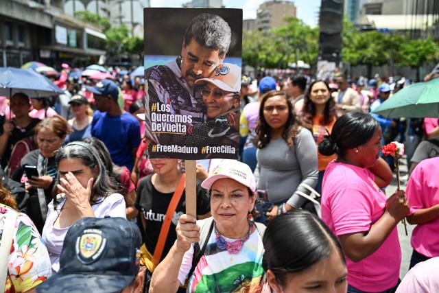 A woman supporter of Venezuela’s interim President Delcy Rodriguez holds a banner with a picture of Venezuela's ousted president Nicolas Maduro and his wife Cilia Flores during a demonstration in Caracas on April 20, 2026, protesting against a rally held by opposition figure Maria Corina Machado in Madrid on April 19, 2026. (Photo by Juan BARRETO / AFP)