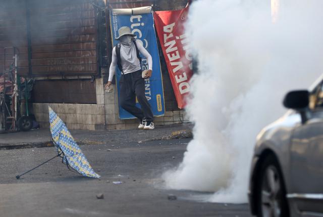 A protester holds stones amid tear gas smoke during a protest against budget cuts to university education near the National Congress in Tegucigalpa on April 20, 2026. (Photo by Johny MAGALLANES / AFP)