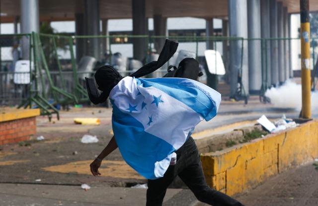 A protester wrapped in the Honduran flag throws stones at police during a protest against budget cuts to university education near the National Congress in Tegucigalpa on April 20, 2026. (Photo by Johny MAGALLANES / AFP)