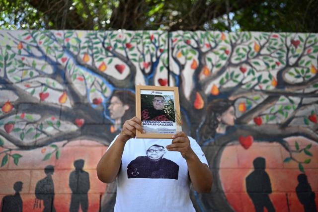 Esmeralda Rosales shows a portrait of her missing brother, Fernando Rosales, during the inauguration of a mural in tribute to disappeared people, at the University of El Salvador, in San Salvador, on March 19, 2026. Thousands of people went missing in the gang wars that throttled El Salvador for decades until President Nayib Bukele cracked down hard four years ago. (Photo by AFP)