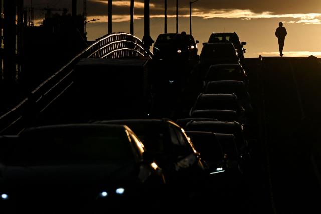 A man on a scooter ride past a traffic jam during sunset in Bogota on April 20, 2026. (Photo by Pablo VERA / AFP)