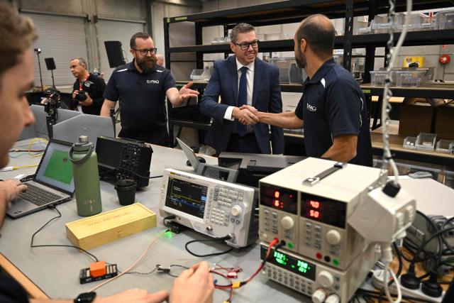 Australia's Minister for Defence Industry Pat Conroy (C) greets staff on the drone production line with SYPAQ Systems chief engineer Ross Osborne (L) as the Australian Government announces it will invest 5 billion USD over the next decade in counter drones for the Australian Defence Force (ADF), in Melbourne on April 21, 2026 (Photo by William WEST / AFP)