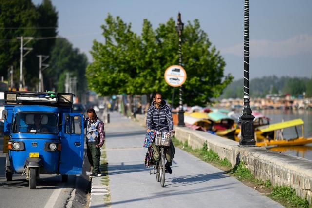 A vendor rides his bicycle along the banks of the iconic Dal Lake in Srinagar on April 21, 2026. In the once-booming resort towns of India-controlled Kashmir, hoteliers are switching on the lights to welcome a trickle of visitors, a year after militants opened fire on holidaymakers in an attack that killed 26 people. (Photo by MANAN VATSYAYANA / AFP)