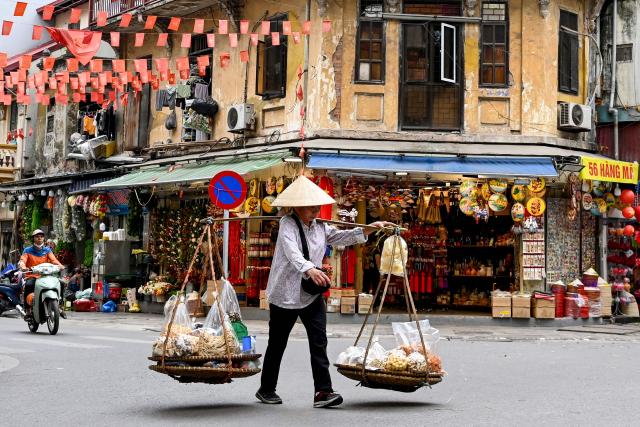 A street vendor walks down a street carrying food for sale in Hanoi on April 21, 2026. (Photo by Nhac NGUYEN / AFP)