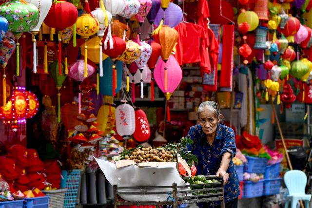 A street vendor pushes a fruit cart as she walks past a lamp shop in Hanoi on April 21, 2026. (Photo by Nhac NGUYEN / AFP)