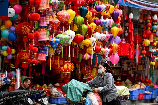 A street vendor pushes her fruit stall as she walks past a lamp shop in Hanoi on April 21, 2026. (Photo by Nhac NGUYEN / AFP)