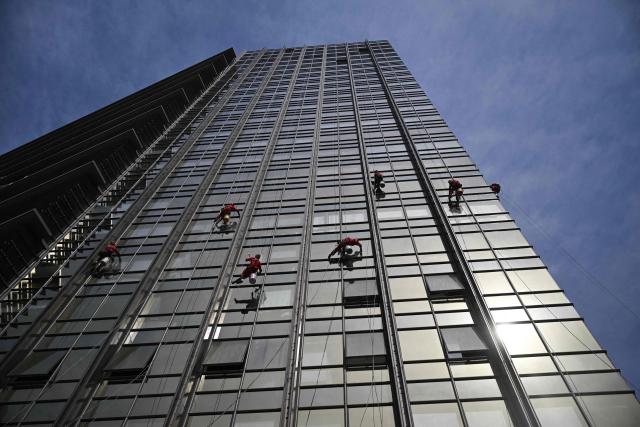 Workers clean the glass facade of a high-rise building in Beijing on April 21, 2026. (Photo by Pedro PARDO / AFP)