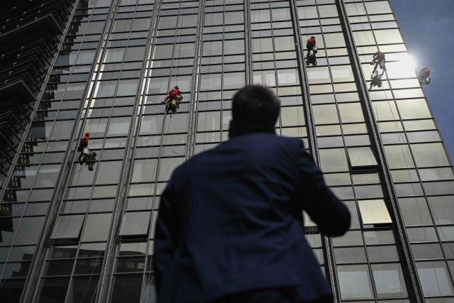 Workers clean the glass facade of a high-rise building in Beijing on April 21, 2026. (Photo by Pedro PARDO / AFP)