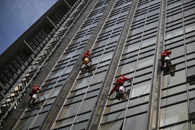 Workers clean the glass facade of a high-rise building in Beijing on April 21, 2026. (Photo by Pedro PARDO / AFP)