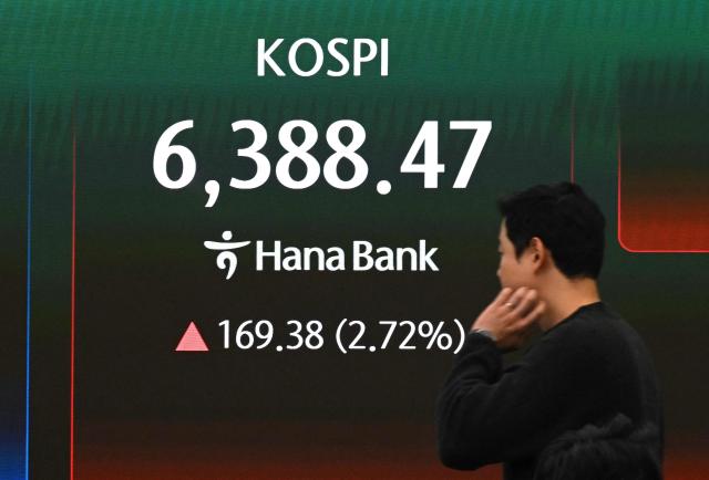 A currency dealer walks past a screen showing South Korea's benchmark stock index (KOSPI) in a foreign exchange dealing room at the Hana Bank headquarters in Seoul on April 21, 2026. South Korea's benchmark Kospi stock index closed at a record high on April 21 as a rally in tech firms helped it recover the steep losses suffered during a rout triggered by the war in the Middle East. (Photo by Jung Yeon-je / AFP)