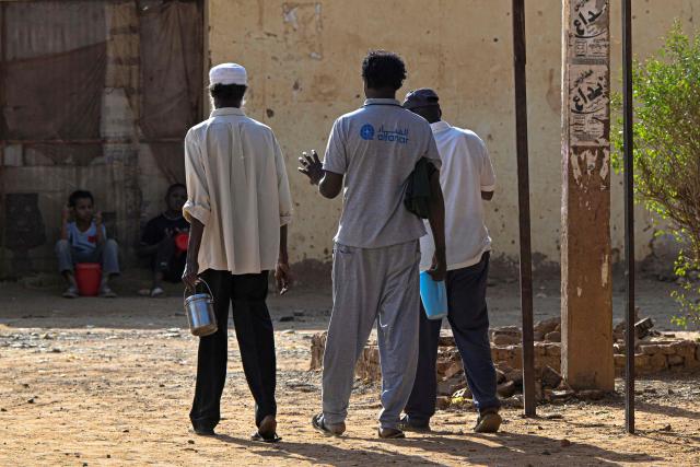 Sudanese men carry their canister filled with free food distributed by the “Community Kitchen” initiative in Omdurman on April 21, 2026. The top United Nations official in Sudan told AFP on April 16, 2026, that the country, facing the world's largest humanitarian crisis, has been "abandoned" as the war between the army and the paramilitary Rapid Support Forces (RSF) enters its fourth year. (Photo by Khaled DESOUKI / AFP)