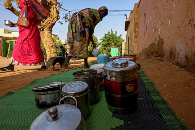 Sudanese women arrange containers filled with free food placed in front of the home of the founder of the “Community Kitchen” initiative, as another take her's away, in Omdurman on April 21, 2026. The top United Nations official in Sudan told AFP on April 16, 2026, that the country, facing the world's largest humanitarian crisis, has been "abandoned" as the war between the army and the paramilitary Rapid Support Forces (RSF) enters its fourth year. (Photo by Khaled DESOUKI / AFP)