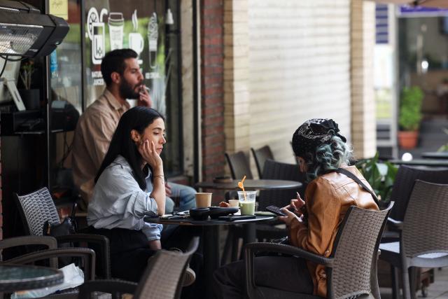TOPSHOT - Two women sit at a cafe table with drinks in Tehran on April 21, 2026, amid a ceasefire in the region. With the end of a two-week ceasefire approaching, the White House said US Vice President JD Vance was ready to return to Pakistan for fresh negotiations to end a conflict that has sent crude soaring and revived inflation fears. (Photo by AFP) / 