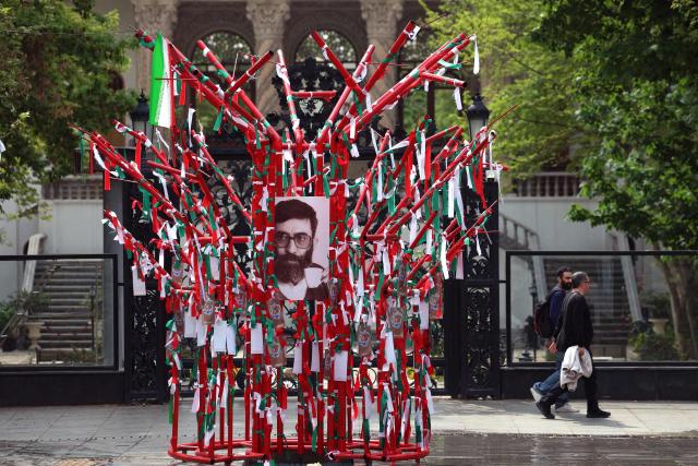 Iranians walk through a park in northern Tehran, passing a structure adorned with the national flag and a portrait of the late Iranian supreme leader Ayatollah Ali Khamenei as a young man, on April 21, 2026, amid a ceasefire in the region. With the end of a two-week ceasefire approaching, the White House said US Vice President was ready to return to Pakistan for fresh negotiations to end a conflict that has sent crude soaring and revived inflation fears. (Photo by AFP) / 