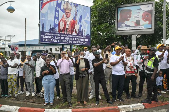 Residents stand next to the road on the route where Pope Leo XIV's motorcade will drive past after his arrival in Malabo on the ninth day of an 11-day apostolic journey to Africa, on April 21, 2026. (Photo by Alberto PIZZOLI / AFP)