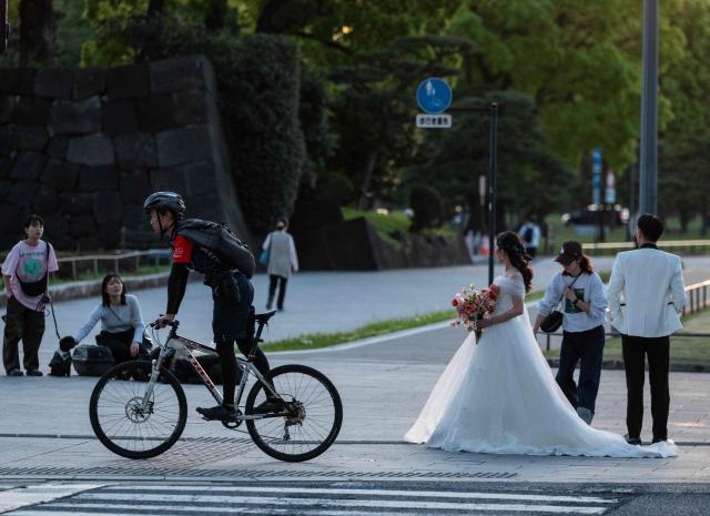 A man bikes past a couple having an evening photo shoot in their wedding outfits in Tokyo on April 21, 2026, near the Tokyo Station complex, one of a number of popular photo spots for newlyweds. (Photo by Andrew CABALLERO-REYNOLDS / AFP)