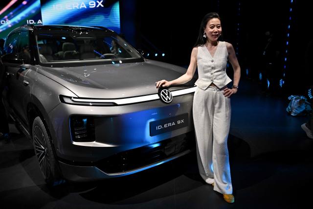 A woman posses next to German automaker Volkswagen's new ID. ERA 9X electric SUV model at an event ahead of the Beijing Auto Show 2026 in Beijing on April 21, 2026. (Photo by Pedro PARDO / AFP)