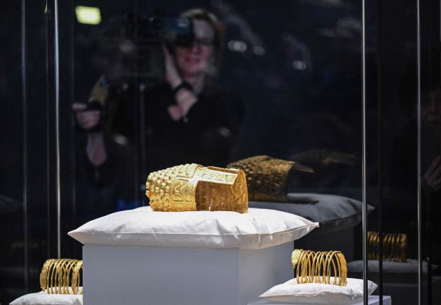 A TV jornalist films the ancient Cotofenesti helmet and two Dacian gold bracelets on display at the National Museum of History of Romania (MNIR) in Bucharest on April 21, 2026. The artifacts, shown together for the first time since their repatriation, are part of a national campaign to bring Romania’s most significant ancient treasures to the public across the country. In January 2025, the Cotofenesti helmet and several gold bracelets were stolen from the Drents Museum in Assen, Netherlands. They were on loan from the National Museum of History of Romania (MNIR) as part of the "Dacia – Empire of Gold and Silver" exhibition. (Photo by Daniel MIHAILESCU / AFP)