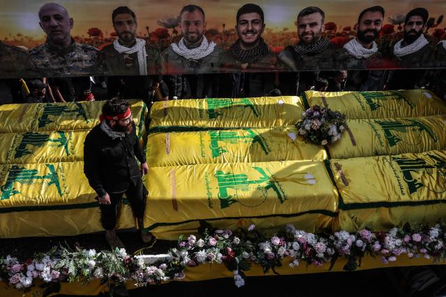 Coffins sit on a trailer beneath portraits of Hezbollah fighters killed before a 10-day ceasefire was agreed between the Iran-backed militant group and Israel during a mass funeral procession in the southern village of Kfar Sir on April 21, 2026. Israeli defence minister said on April 21 that his country's campaign in Lebanon relied on both military and diplomatic pressure to disarm Iran-allied Hezbollah. Though a truce between Israel and Lebanon took effect on April 17, Israeli troops are still present and actively fighting Hezbollah militants in Lebanon's south. (Photo by Anwar AMRO / AFP)