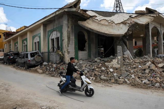 A youth rides a moped past a mosque that was targeted in an Israeli strike in the southern Lebanese village of Kfar Sir on April 21, 2026. Israeli defence minister said on April 21 that his country's campaign in Lebanon relied on both military and diplomatic pressure to disarm Iran-allied Hezbollah. Though a truce between Israel and Lebanon took effect on April 17, Israeli troops are still present and actively fighting Hezbollah militants in Lebanon's south. (Photo by Anwar AMRO / AFP)