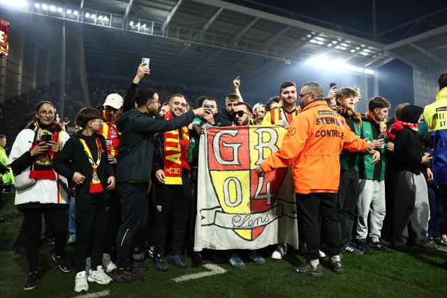 Supporters of Lens celebrate on the pitch after their team's victory at the end of the French Cup semi-final football match between and RC Lens and Toulouse FC at the Stade Bollaert-Delelis in Lens, northern France on April 21, 2026. (Photo by Sameer AL-DOUMY / AFP)
