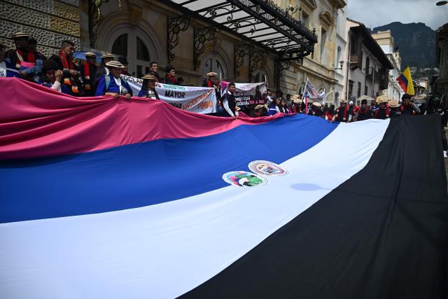 Misak Indigenous people hold a large flag during a protest to demand compliance with agreements reached with the government regarding their territories outside the Ministry of Foreign Affairs in Bogota on April 21, 2026. (Photo by Raul ARBOLEDA / AFP)