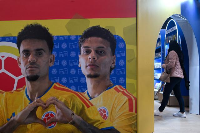 A woman walks next to a banner featuring images of Colombian footballers Luis Diaz (L) and Richard Rios at the International Book Fair in Bogota on April 21, 2026. (Photo by Raul ARBOLEDA / AFP)