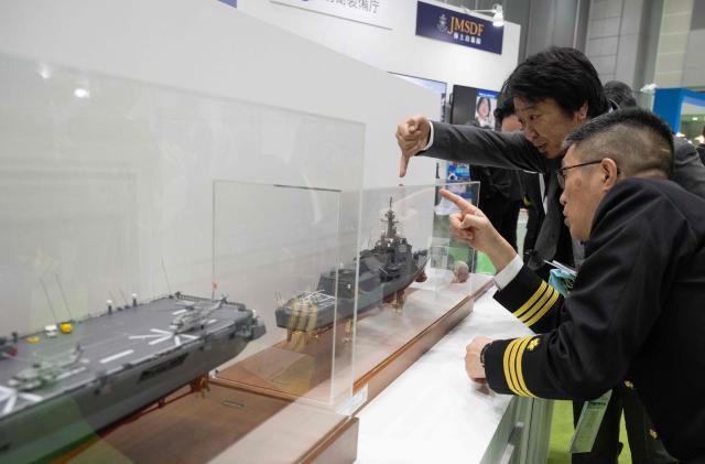 A member of the Japanese Maritime Self Defence Force (JMSDF) team (R) speaks with an attendee at their booth at the Sea Japan Maritime Exhibition and Conference in Tokyo on April 22, 2026. Japan will ease decades-old arms export curbs, the government said Tuesday, in a major policy shift that paves the way for the sale of lethal weapons overseas as Tokyo ramps up its defence ambitions. The new rules end Japan's self-imposed curb on sales of lethal arms as Tokyo seeks to enter the international arms market, hoping to bolster national defence as well as boost economic growth. (Photo by Andrew CABALLERO-REYNOLDS / AFP)