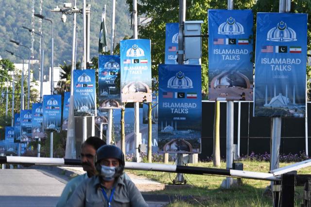 Motorcyclists ride past posters highlighting Pakistan's mediation of Iran–US peace talks near the Serena Hotel at the Red Zone area in Islamabad on April 22, 2026. Pakistani Prime Minister Shehbaz Sharif thanked US President Donald Trump on April 22, for extending a ceasefire with Iran that had been soon set to expire and urged both sides to continue talks. (Photo by Aamir QURESHI / AFP)
