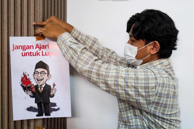 An activist puts up a poster that reads "do not teach us to forget" and features a caricature of Culture Minister Fadli Zon, ahead of a press conference at the National Commission on Violence Against Women (Komnas Perempuan) office in Jakarta on April 22, 2026. (Photo by BAY ISMOYO / AFP)
