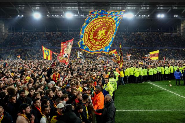 Cordoned by stewards, Lens supporters celebrate their team's victory on the pitch at the end of the French Cup semi-final football match between RC Lens and Toulouse FC at the Stade Bollaert-Delelis in Lens, northern France, on April 21, 2026. (Photo by Sameer AL-DOUMY / AFP)