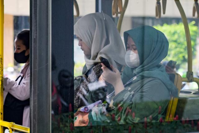 Passengers occupy themselves with their smartphones on a public bus in Jakarta on April 22, 2026. (Photo by BAY ISMOYO / AFP)