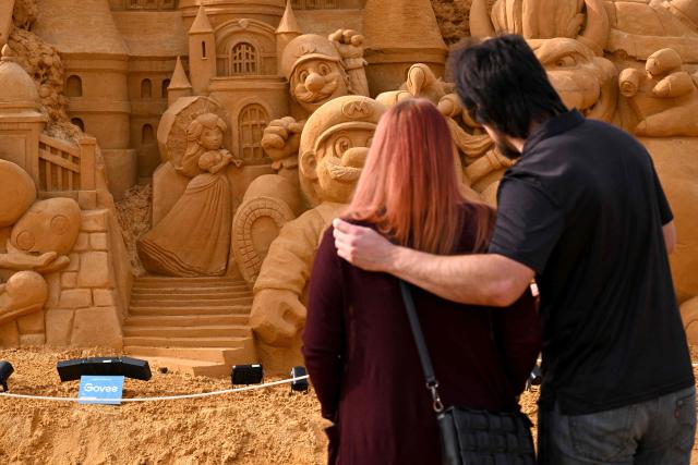 A couple look at a giant sand sculpture of the Super Mario Bros at the entrance to the Australian Sand Sculpting Championships in Melbourne on April 22, 2026. More than 400 tonnes of sand has be used by artists to carve 18 large-scale masterpieces. (Photo by William WEST / AFP)