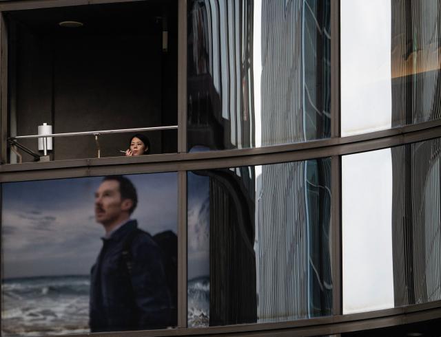 A woman smokes as an advertisement with British actor Benedict Cumberbatch is reflected in the window below in Tokyo on April 22, 2026. (Photo by Andrew CABALLERO-REYNOLDS / AFP)