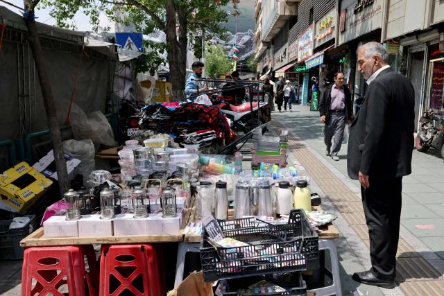 Iranians walk past a stall erected on a sidewalk in central Tehran on April 22, 2026, amid a regional ceasefire. Pakistan's capital was still locked in gear on April 22, to host high-stakes US-Iran talks that were pushed back at the last minute overnight, but many residents began to tire of the heavy personal and economic toll of tight security restrictions. (Photo by ATTA KENARE / AFP) / 