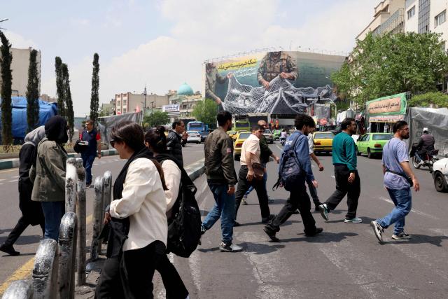 Iranians walk across a zebra crossing past a giant billboard reading 'The Strait of Hormuz remains closed' at the Revolution Square in Tehran on April 22, 2026, amid a ceasefire in the region. Pakistan's capital was still locked in gear on April 22, to host high-stakes US-Iran talks that were pushed back at the last minute overnight, but many residents began to tire of the heavy personal and economic toll of tight security restrictions. (Photo by ATTA KENARE / AFP) / 