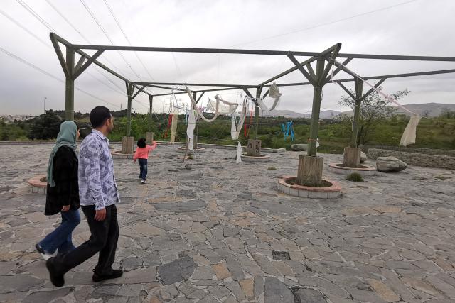 A child looks up at a fabric installation as her parents watch in Pardisan Park in northern Tehran on April 22, 2026, amid a regional ceasefire. Pakistan's capital was still locked in gear on April 22, to host high-stakes US-Iran talks that were pushed back at the last minute overnight, but many residents began to tire of the heavy personal and economic toll of tight security restrictions. (Photo by ATTA KENARE / AFP) / 