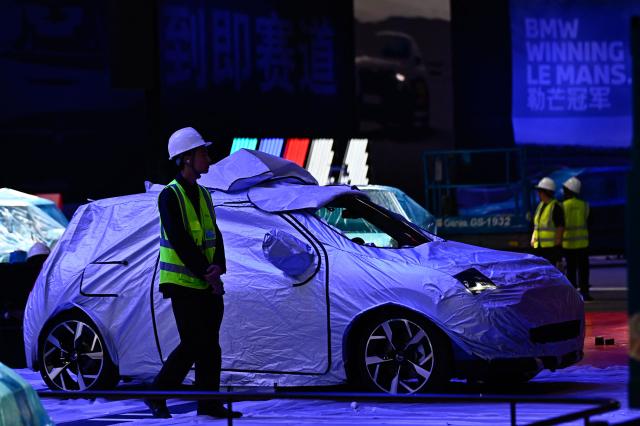 A covered Mini car is seen as workers assemble the stand for German carmaker BMW ahead of the Beijing Auto Show 2026 at the China International Exhibition Center in Beijing on April 22, 2026. (Photo by Pedro PARDO / AFP)