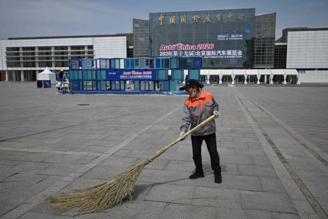 A worker sweeps the esplanade at an entrance of the venue ahead of the Beijing Auto Show 2026 at the China International Exhibition Center in Beijing on April 22, 2026. (Photo by Pedro PARDO / AFP)