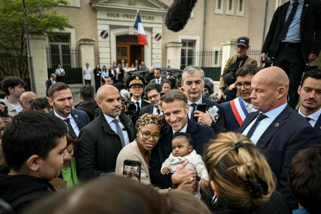 France's President Emmanuel Macron poses for a photograph with a woman and a baby as he leaves after chairing a weekly cabinet meeting in the central France city of Montluçon on April 22, 2026. (Photo by Jeff PACHOUD / POOL / AFP)