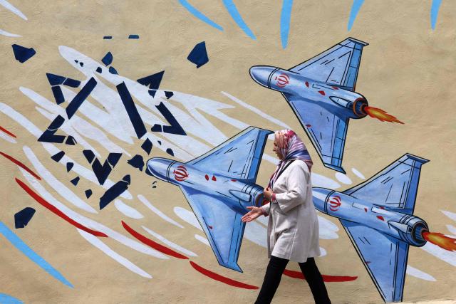 This photo taken on April 8, 2026 shows a woman walking past an anti-USA and anti-Israel mural, in Tehran. Since the outbreak of war between Iran, Israel and the United States, colourful murals have sprung up across Tehran and beyond, rich in symbolism and themes of resistance and defiance. Murals and banners have long been a defining feature of Iran's urban landscape, particularly in Tehran, where such paintings in central squares often mirror the state's political messaging and foreign policy stance. (Photo by ATTA KENARE / AFP) / Attention editors: AFP covers the war in the Middle East through its extensive regional network, including bureaus in Tehran, Jerusalem and several neighboring countries.Since the start of the conflict, journalists have been working under increasingly restrictive conditions. Authorities in several countries have limited reporters movements, photo and live video coverage from sensitive locations. Some governments and armed groups have banned images of missile or drone strikes and other security-related sites. / 