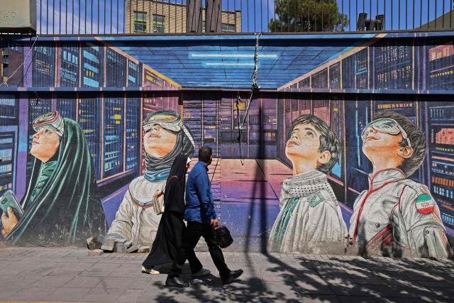 This photo taken on April 12, 2026 shows people walking past a wall mural along the roadside in Tehran. Since the outbreak of war between Iran, Israel and the United States, colourful murals have sprung up across Tehran and beyond, rich in symbolism and themes of resistance and defiance. Murals and banners have long been a defining feature of Iran's urban landscape, particularly in Tehran, where such paintings in central squares often mirror the state's political messaging and foreign policy stance. (Photo by ATTA KENARE / AFP) / Attention editors: AFP covers the war in the Middle East through its extensive regional network, including bureaus in Tehran, Jerusalem and several neighboring countries.Since the start of the conflict, journalists have been working under increasingly restrictive conditions. Authorities in several countries have limited reporters movements, photo and live video coverage from sensitive locations. Some governments and armed groups have banned images of missile or drone strikes and other security-related sites. / 