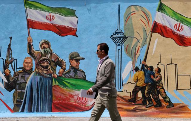 This photo taken on April 8, 2026 shows a man walking past an anti-USA and anti-Israel mural, in Tehran. Since the outbreak of war between Iran, Israel and the United States, colourful murals have sprung up across Tehran and beyond, rich in symbolism and themes of resistance and defiance. Murals and banners have long been a defining feature of Iran's urban landscape, particularly in Tehran, where such paintings in central squares often mirror the state's political messaging and foreign policy stance. (Photo by ATTA KENARE / AFP) / Attention editors: AFP covers the war in the Middle East through its extensive regional network, including bureaus in Tehran, Jerusalem and several neighboring countries.Since the start of the conflict, journalists have been working under increasingly restrictive conditions. Authorities in several countries have limited reporters movements, photo and live video coverage from sensitive locations. Some governments and armed groups have banned images of missile or drone strikes and other security-related sites. / 