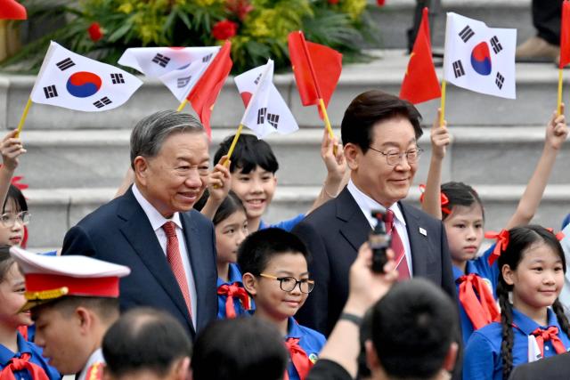 Vietnam's President To Lam (L) and South Korean President Lee Jae Myung (R) pose for photos with children waving flags during a welcoming ceremony at the Presidential Palace in Hanoi on April 22, 2026. (Photo by Nhac NGUYEN / POOL / AFP)
