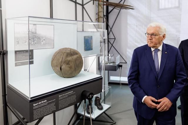 German President Frank-Walter Steinmeier looks at an old medicine ball displayed under the topic 'sport as a punishment' during the exhibition at the memorial site of the former Closed Youth Detention Centre (Geschlossener Jugendwerkhof Torgau - GJWH) in Torgau, eastern Germany on April 22, 2026. According to the memorial site, the closed youth detention centre used to be the only closed residential care facility in the GDR, where young people were to be re-educated into "socialist personalities" within just a few months. During the course of GDR history, approximately 135,000 children and young people were forced to go through socialist re-education practices in youth work camps and special children's homes. Historical traces at the memorial site are visible in the former solitary confinement cells and courtyard. (Photo by Jens SCHLÜTER / POOL / AFP)