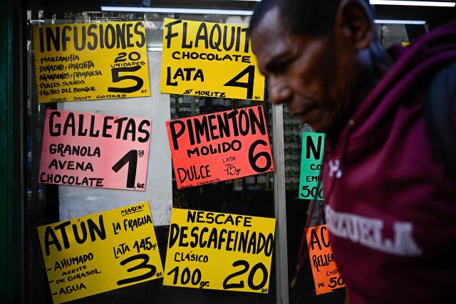 A man walks past a supermarket displaying signs with food prices in US dollars in Caracas on April 22, 2026. (Photo by Federico PARRA / AFP)