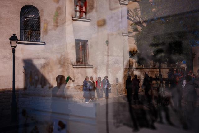 Tourists are reflected in a gallery window as they stroll up the Montmartre hill in Paris on April 22, 2026. (Photo by Dimitar DILKOFF / AFP)