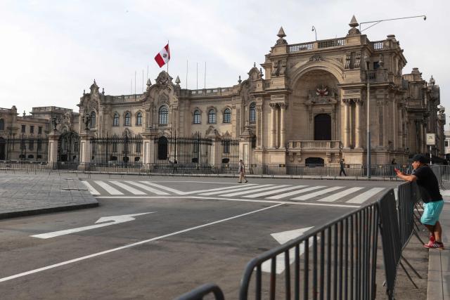 A man checks his mobile phone at Plaza Mayor with the Government Palace in the background in Lima on April 22, 2026. Peru's foreign and defense ministers resigned on April 22 in protest over the interim president's decision to stall a $3.5 billion deal for the purchase of 24 US F-16 fighter jets. (Photo by Connie FRANCE / AFP)